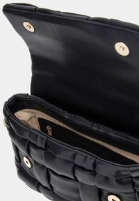 Borsa a tracolla nera trapuntata con una texture liscia, accessori in oro e un ampio interno beige, dotata di una tasca con zip per l'organizzazione.