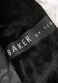 Sort faux fur tekstur med en blød finish. Etiketten læser "BAKER BY TED" i hvidt på et sort bånd. Har lysfarvede fabriksakcenter.