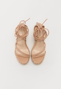 Nude espadrillesandaler med kryssede stropper, en flettet jute kilehæl og dekorative båndsløyfer festet foran. Flat såle.