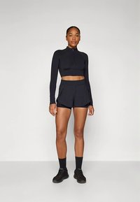 Melns īss crop top ar garām piedurknēm un priekšā rāvējslēdzēju, kopā ar saskaņotām melnām šortām ar krokām. Modele valkā melnas kurpes un zeķes.