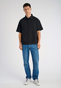 Czarna koszulka polo z krótkim rękawem, z kołnierzykiem i trzema guzikami, w połączeniu z niebieskimi dżinsami prostymi i białymi trampkami.