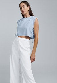 Lyseblå cropped top med ærmeløst design og sidebindinger, parret med hvide vide bukser i tekstureret stof.