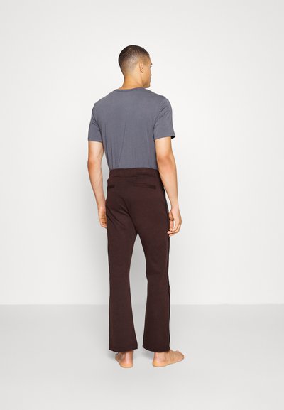 Conjunto casual masculino com uma t-shirt cinza e calças flare castanhas de textura suave, com detalhes mínimos e sem peças de metal visíveis.