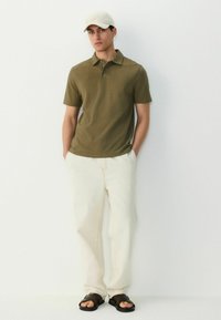 Oliven grøn polo shirt med korte ærmer og subtil tekstur, parret med kreme-farvede bukser og brune sandaler. Simpelt, afslappet design.