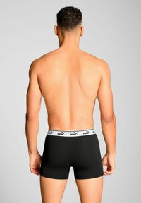 Black boxer shorts made of soft material with a white elastic waistband featuring the Puma logo. The fit is snug and tailored.