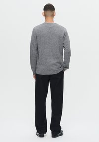 Gray knit sweater with crew neck, featuring a relaxed fit and ribbed cuffs, paired with black trousers and black shoes.