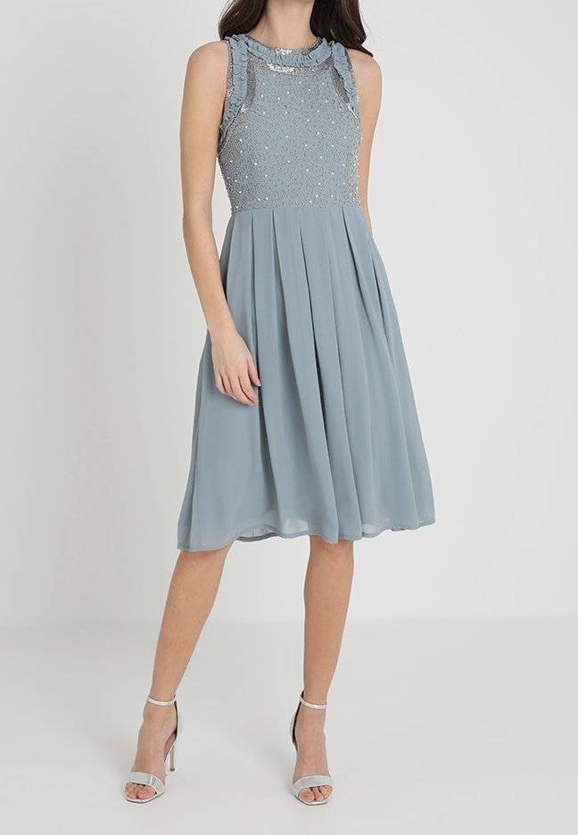 En ljusblå ärmlös klänning med en texturerad överdel, dekorerad med paljetter, och en flödande plisserad kjol. Silverfärgade klackar fulländar looken.