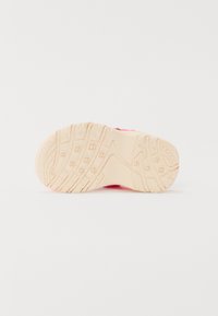 Ulkopohja urheilukengistä vaaleanbeigessä kumissa. Teksturoitu pinta, jossa on uria ja lukuja pidon parantamiseksi. Kirkkaan vaaleanpunaiset yksityiskohdat näkyvät reunoilla.