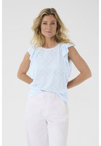 Top ricamato azzurro chiaro con maniche a balze, motivi floreali tagliati al laser e orlo ondulato; abbinato a pantaloni di colore chiaro.