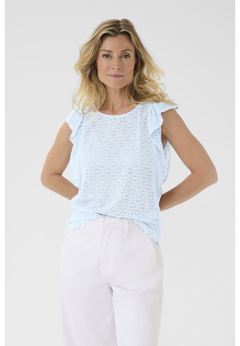 Top ricamato azzurro chiaro con maniche a balze, motivi floreali tagliati al laser e orlo ondulato; abbinato a pantaloni di colore chiaro.