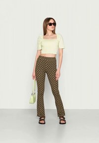Top cropped verde claro com mangas bufantes, combinado com calças flare estampadas castanhas. Acessórios incluem uma bolsa verde e óculos de sol escuros.