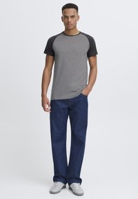 Gray short-sleeve t-shirt with black raglan sleeves, paired with dark blue straight-leg jeans and gray sneakers. Minimal design.