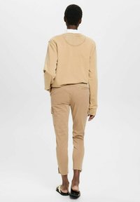 Beige sweatshirt med rund halsringning, kombinerad med beige cargo-byxor som har sidofickor, och öppetåiga sandaler.