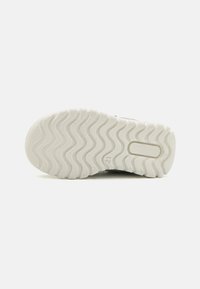 Suola di sneaker bianca con un motivo a onde e un'intaglio rettangolare; dotata di numeri e una superficie in gomma testurizzata per una miglior presa.