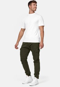 T-shirt bianca in cotone abbinata a pantaloni cargo verde oliva con molte tasche. Il modello indossa sneakers bianche alte.