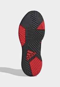 Suela de zapatilla deportiva negra y roja que presenta un patrón texturizado con surcos en zigzag y acentos hexagonales; marcada con "adidas" en el lateral.