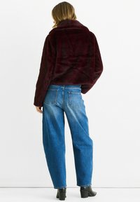 Burgundy faux fur jacket with a high collar, paired with loose-fitting blue jeans. Black ankle boots complete the outfit.