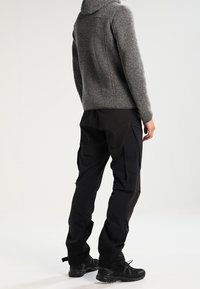 Szara dziergana bluza z kapturem z wysokim kołnierzem, w połączeniu z czarnymi spodniami cargo z kieszeniami. Całość uzupełniają czarne buty.