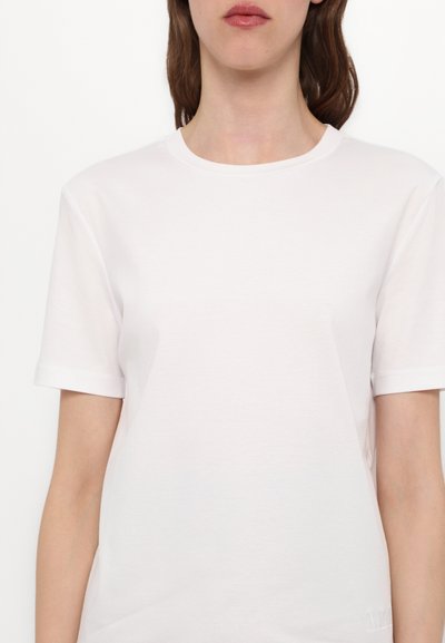 Bela majica s kratkimi rokavi iz gladkega bombažnega materiala, z okroglim izrezom in diskretnim logotipom na robu.