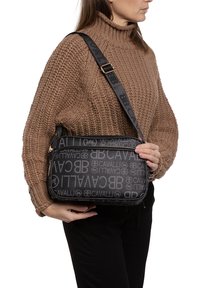 Borsa a spalla nera con design del logo testurizzato, chiusura con zip e tracolla regolabile. Presenta dettagli in hardware dorato e una forma rettangolare.