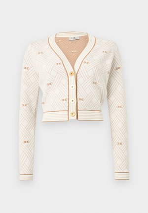 Trumpas kreminės spalvos megztinis su ilgomis rankovėmis, smėlio spalvos austas raštas, auksiniai mygtukai ir ribinė apdaila ant rankogių, apačios ir kaklo srities.