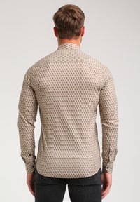 Camisa de manga larga en un patrón geométrico de color beige y crema, con cuello tipo button-down y botones en los puños, elaborada con una tela suave.
