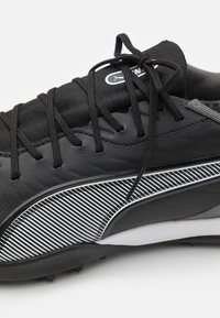 Black athletic shoe featuring a textured leather upper, black laces, and a white striped pattern along the side for added detail.