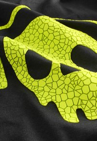 Fekete anyag, textúrált neon zöld mintával, amely pikkelyekhez hasonlít, nagy, koponya alakú kivágásokkal.