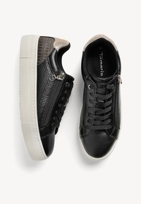 Baskets en cuir noir avec panneaux latéraux texturés, semelles épaisses blanches, zips latéraux, lacets noirs et accents beiges au talon, nom de la marque à l'intérieur.