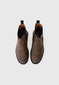 Stivali ankle in pelle marrone con una superficie liscia, pannelli laterali elastici e linguette. Suole in gomma nera che offrono aderenza e stabilità.