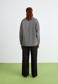 Camicia di denim grigia con vestibilità comoda, maniche lunghe e polsini con bottoni, abbinata a pantaloni neri a gamba larga e scarpe multicolori.