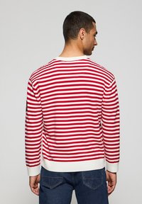 Rood-wit gestreepte trui, gebreid materiaal, ronde hals, ribgebreide mouw- en onderrand, zijlogo-patch, casual fit. Zicht van achter.
