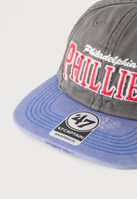 Γκρι και μωβ καπέλο snapback των Philadelphia Phillies με κόκκινο κεντητό κείμενο και αυτοκόλλητο '47 Captain στην κορυφή της γείσο.