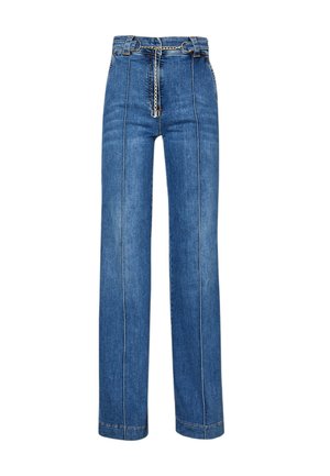 Kobieta w czarnym prążkowanym crop topie, niebieskich szerokich dżinsach z wysokim stanem z łańcuszkowym paskiem oraz sandałach na obcasie z odkrytymi palcami, stoi z rękami w kieszeniach.