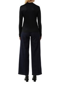 Czarna bluzka z długim rękawem połączona z szerokimi ciemnoniebieskimi dżinsami. Gładka faktura, minimalistyczny design i widoczne akcenty u dołu. Czarne buty na obcasie.