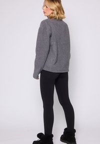 Maglione grigio lanoso con vestibilità rilassata, orlo arrotondato e maniche lunghe, abbinato a leggings neri e stivali alla caviglia neri foderati in pelliccia.