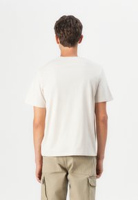 Cremefarvet bomulds t-shirt med klassisk rund hals og korte ærmer, set bagfra. Enkel, udekoreret design.