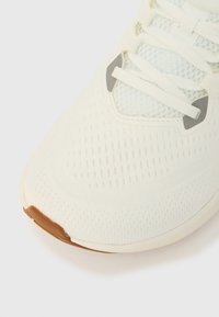 Tuvplāns ar baltu sporta apavu, kas izgatavots no tīkliņa materiāla augšdaļas, baltas mežģīnes un brūnu gumijas apzīmējumu uz pirkstgala uz gaiša fona.