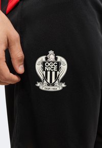 Main près d'un tissu noir avec le logo du club de football OGC Nice présentant un aigle couronné et le texte "Despi 1904."