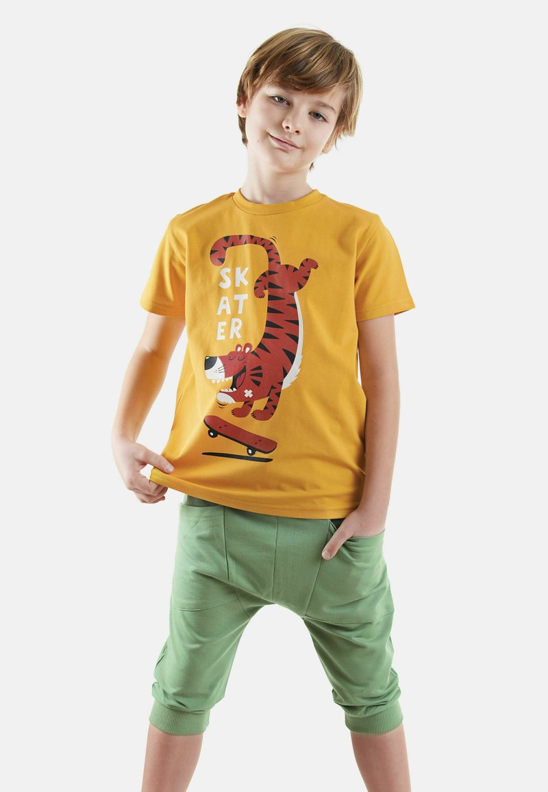 Gul bomulds t-shirt med en rød tiger grafik og teksten "SKATER," parret med lysegrønne cropped bukser med opkrøllede kanter.