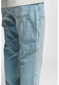 Light blue denim cargo pants with a relaxed fit, featuring visible stitching, side pockets, and a textured fabric finish.