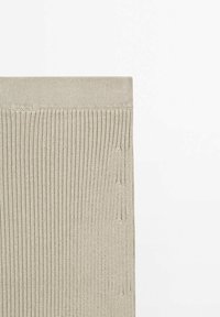 Gros plan d’un tissu tricoté côtelé beige avec un motif vertical et un ourlet plié le long du bord supérieur sur un fond blanc.