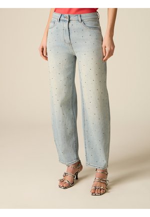 Lichtblauwe high-waist jeans met kleine strass-steentjes, gedragen met slangenprint sandalen met hak en smalle bandjes.