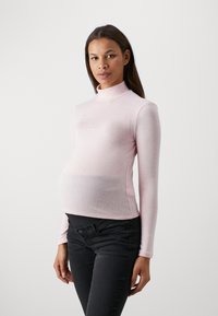 Dolcevita in rosa pallido, design aderente, maniche lunghe, texture morbida, abbinato a jeans scuri, che mette in evidenza un pancione arrotondato.