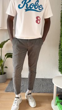 White t-shirt with blue "Kobe" text and red number 8, paired with textured gray trousers and white sneakers, standing on wooden floor.