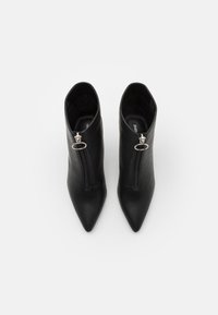 Paire de bottines en cuir noir à bout pointu avec fermetures éclair à l'avant et tirettes rondes argentées, vue de dessus sur fond blanc.