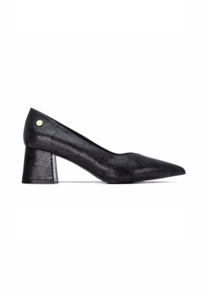 Zapato de mujer negro de cuero texturizado con tacón bajo de bloque y pequeño emblema dorado redondo cerca del tacón sobre fondo blanco.