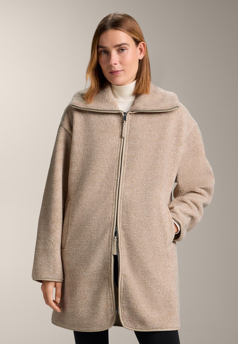 Beige fleece jas met een hoge kraag, ritssluiting aan de voorkant, lange mouwen en zijzakken. Gestructureerde stof en een ontspannen silhouet.