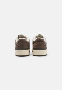 Brown suede sneakers with a cream-colored sole, featuring a padded collar and heel, and contrasting stitching details.