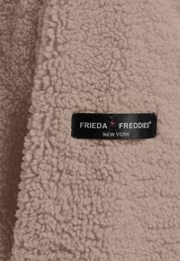 Lichtroze fleece stof met een gestructureerd, zacht oppervlak. Bevat een zwart label met witte tekst "FRIEDA FREDDIES NEW YORK."